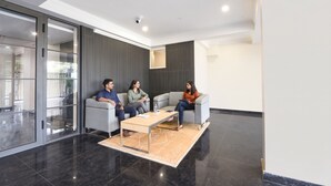 A modern interior with three people seated on sofas, a glass partition, and a ceiling-mounted security camera. - FabHotel Prime Hush & Suites - Manesar and Sector 86 (Gurugram)