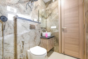 A bathroom with a toilet, sink, shower, and wooden door. - Fabhotel Prime Hush & Suites (Gurugram)