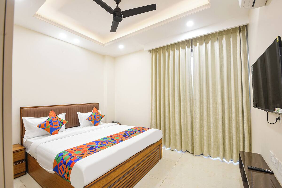 A hotel room with a bed, a ceiling fan, a TV, and a window with curtains.