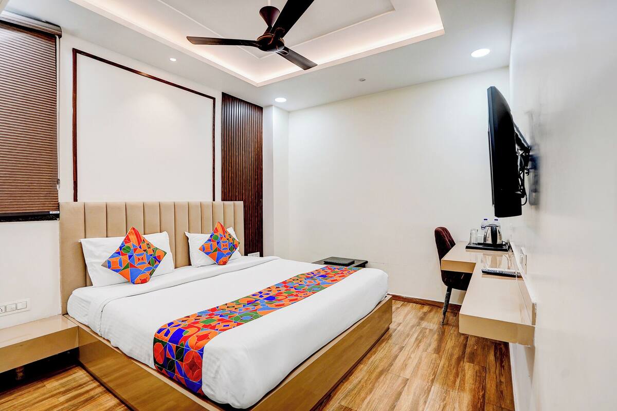 A modern bedroom with a bed, bedside tables, a desk, a chair, a ceiling fan, and a TV mounted on the wall.