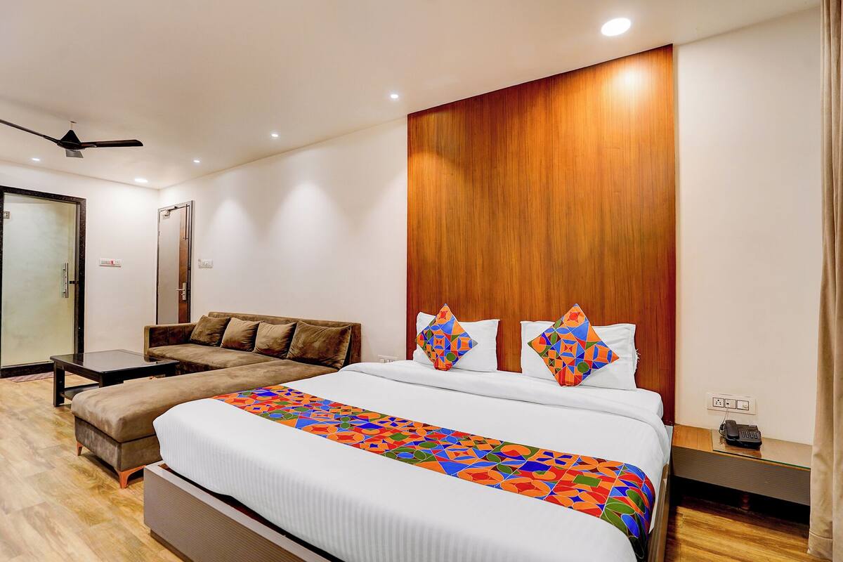 A modern hotel room with a large bed, a sofa, a wooden accent wall, and a ceiling fan.