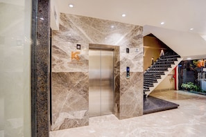 An elevator with a marble wall, a staircase with a red railing, and a digital display. - FabHotel Prime Kartar Grand - Nr. Fazalganj Chauraha (Kanpur)