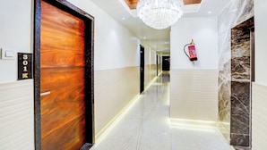 Un pasillo de hotel con una puerta de madera, un extintor y una araña.