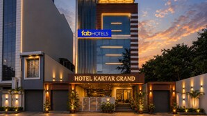 Fachada moderna de hotel con un cartel llamativo que dice 'fabHOTELS HOTEL KARTAR GRAND' y una entrada bien iluminada.