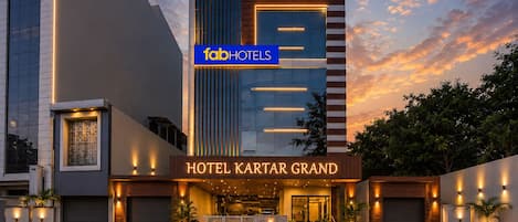 Fachada moderna de hotel con un cartel llamativo que dice 'fabHOTELS HOTEL KARTAR GRAND' y una entrada bien iluminada.