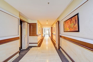 A hotel hallway with marble flooring, wooden paneling, and framed artwork on the walls.