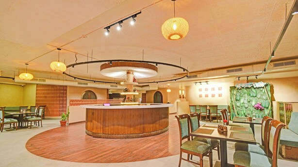 A restaurant with a central wooden bar, round tables, and chairs, with a green wall and ceiling lights. - FabHotel La Vista In Kothapet (Hyderabad)