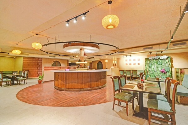 A restaurant with a central wooden bar, round tables, and chairs, with a green wall and ceiling lights. - FabHotel La Vista In Kothapet (Hyderabad)