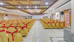Ein großer Saal mit Reihen von Stühlen, einer Bühne und einer hohen Decke mit Beleuchtung.