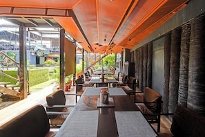 An indoor dining area with tables and chairs, a view of the outdoors, and a modern architectural design. - Fabhotel Prime Surabhi Elite (Hyderabad)