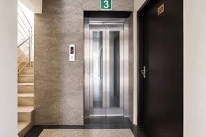 Un ascensor con una pantalla digital, un letrero con el número 3 en la parte superior y una puerta oscura con el número 303.