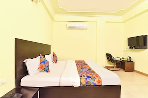 A hotel room with a bed, a desk, a chair, a television, and an air conditioning unit.