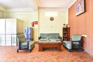 Una sala de estar con un sofá, dos sillones, una mesa de centro, una estantería, un reloj y un extintor.