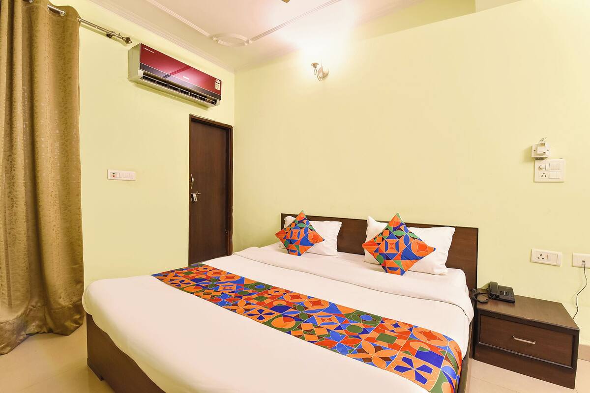A bedroom with a bed, a nightstand, a telephone, a wall-mounted air conditioner, and a door.