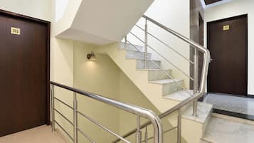 Una escalera con barandales de metal, una lámpara fijada a la pared y dos puertas con los números '302' y '303'.