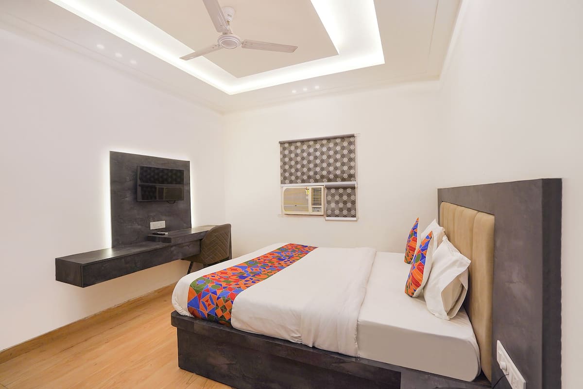 Un dormitorio con cama, escritorio, ventilador de techo, televisor y aire acondicionado.