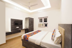 A bedroom with a bed, a TV mounted on the wall, a ceiling fan, and an air conditioning unit. - Fabhotel Roomers (Varanasi)
