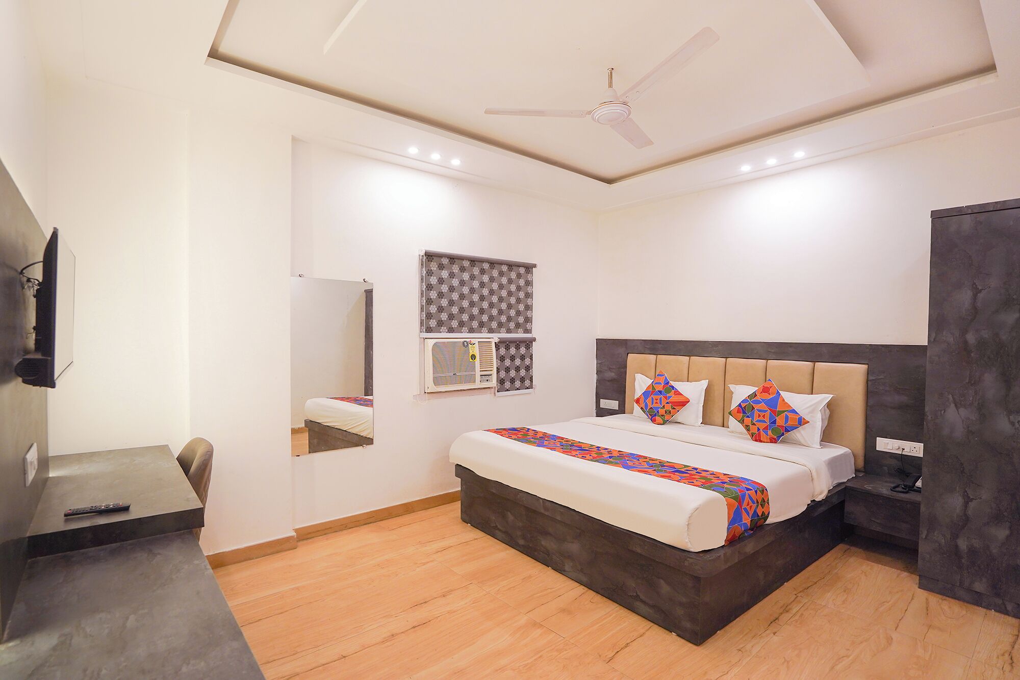 A bedroom with a bed, a ceiling fan, a TV, and a window with blinds.