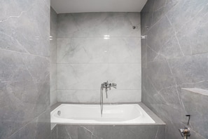 Un baño moderno con una bañera independiente, paredes de mármol y un cabezal de ducha.