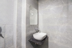 A bathroom with a white sink on a dark countertop, a mirror, and grey marble walls.