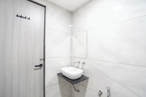 Un baño con un lavamanos blanco, ducha y puerta con pomo.