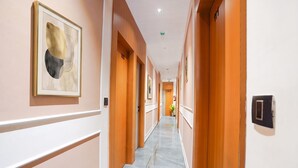 Passadís d'hotel amb portes de fusta, una obra d'art abstracta emmarcada i un paviment de marbre.
