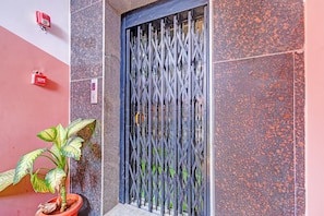 A metal gate with a digital display, a potted plant, and a red emergency box on a building facade.