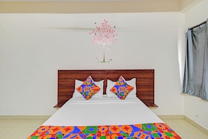 A bedroom with a bed, pillows, a wooden headboard, a wall mural, and a window with curtains.