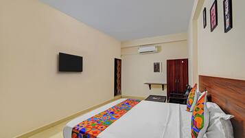 Quarto de hotel com cama, televisão de tela plana, ar condicionado, guarda-roupa e uma mesa pequena.