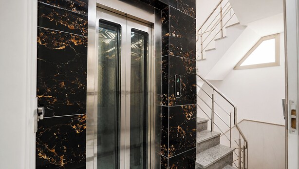 Un ascensor moderno con pantalla digital, una escalera con barandillas de metal y un tragaluz.