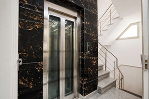 A modern elevator with a digital display, a staircase with metal railings, and a skylight. - Fabhotel Shelter Inn (New Delhi)