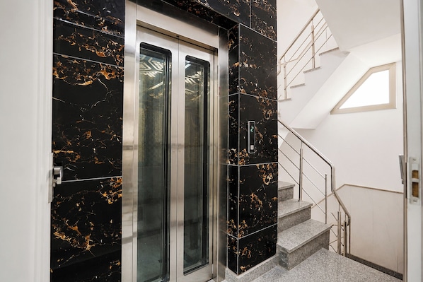 A modern elevator with a digital display, a staircase with metal railings, and a skylight. - Fabhotel Shelter Inn (New Delhi)