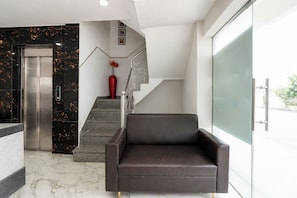 En modern entréhall med ett marmorgolv, en mörk lädersoffa, en trappa med en röd vas och en vägg av glas.