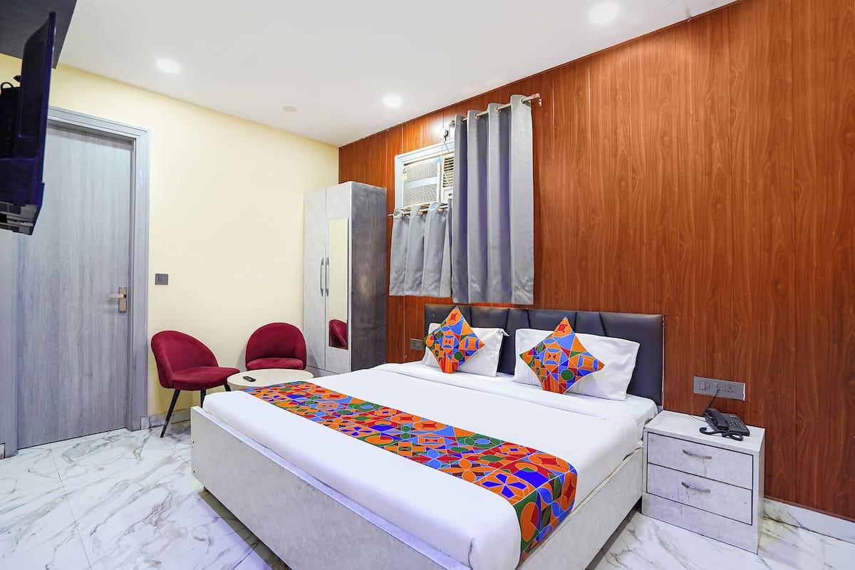 A bedroom with a bed, two red chairs, a wardrobe, a bedside table with a phone, and a window with curtains.