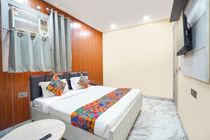 A hotel room with a bed, a small table, a TV, and a window with curtains. - Fabhotel Shelter Inn (New Delhi)