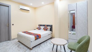 Una habitación de hotel con cama, una mesa redonda, una silla verde, un armario y un equipo de aire acondicionado.