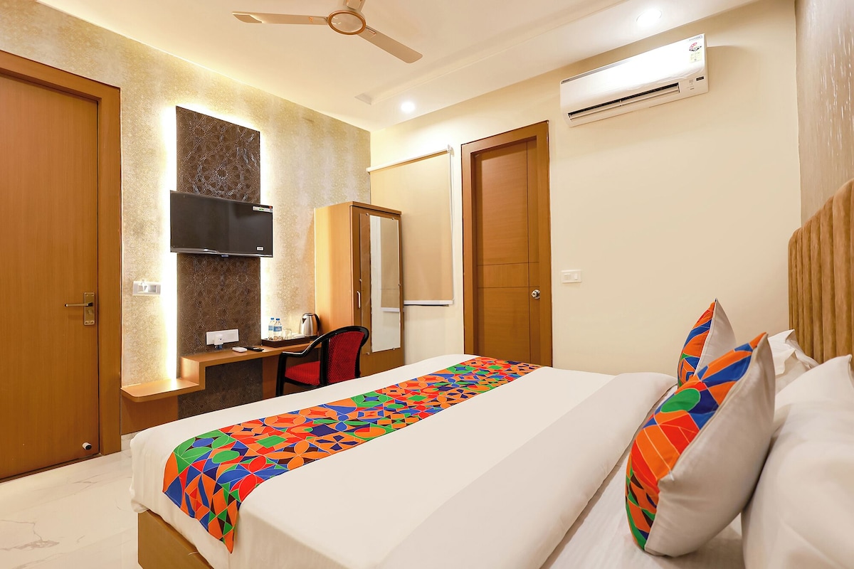 A hotel room with a bed, a desk, a chair, a television, and an air conditioning unit.