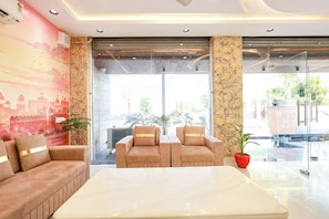 A lobby with a sofa, chairs, a table, a mural, and a large window. - Fabhotel Shree Priyasharnam (Vrindavan)