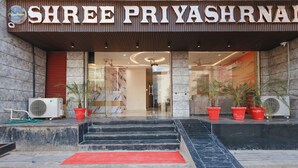 Indgangen til Shree Priyashrnan Hotel med en marmorfacade, rød løber og potteplanter.
