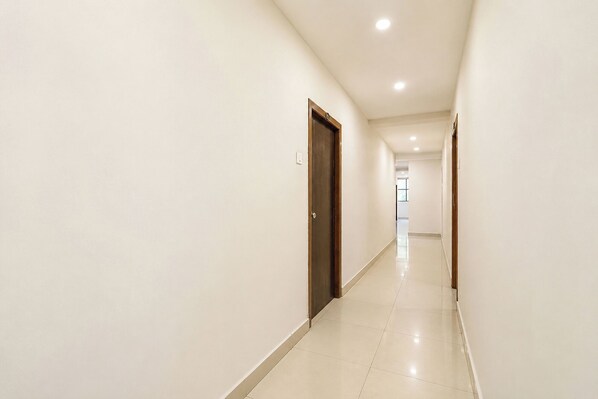 A long, narrow hallway with white walls and a tiled floor, leading to a door at the end.