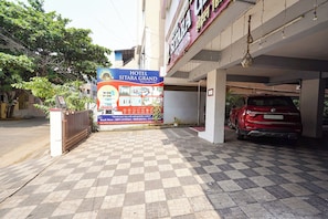 A hotel entrance with a checkered pavement, a red car parked inside, and a large sign advertising the hotel.