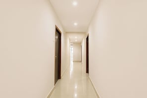 A long, narrow hallway with doors on both sides, leading to a bright room at the end.