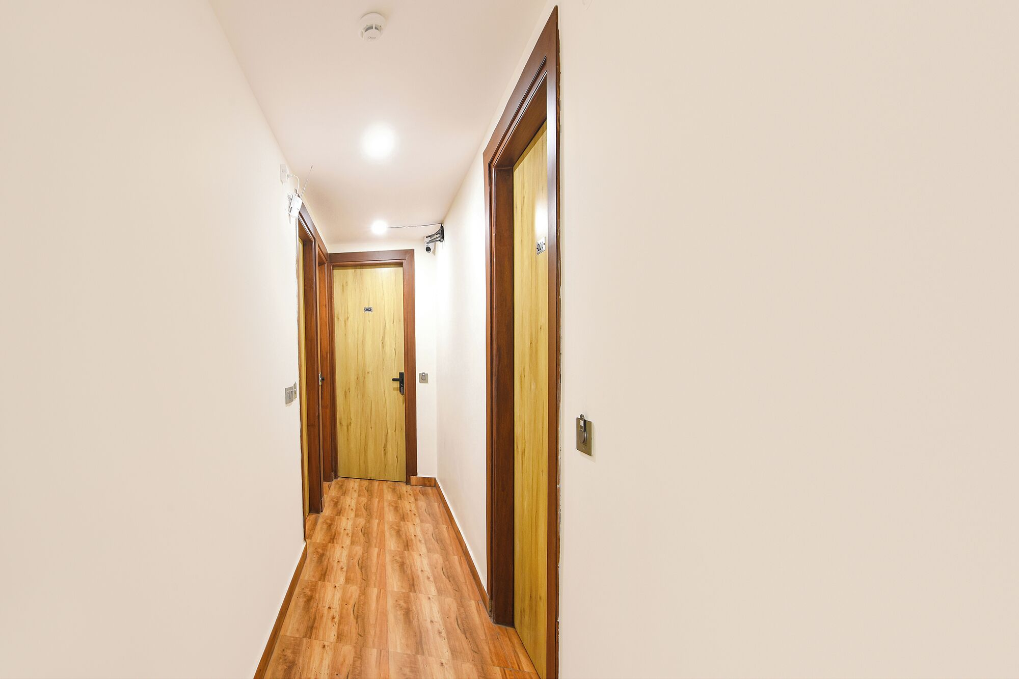 A hallway with wooden flooring, a wooden door at the end, and a light fixture on the ceiling.