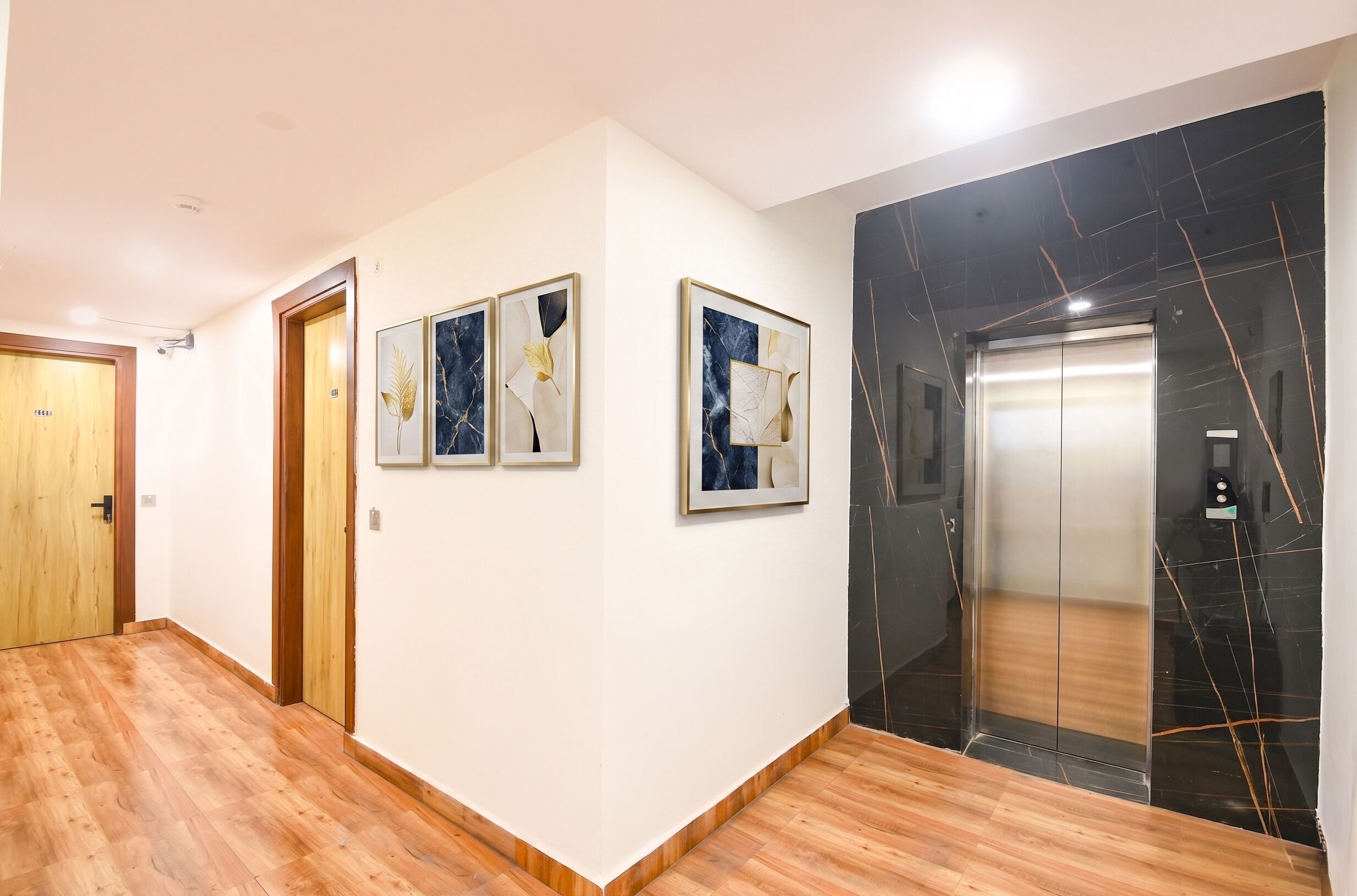 A hallway with wooden flooring, a wooden door, and a marble elevator.