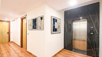 A hallway with wooden flooring, a wooden door, and a marble elevator.