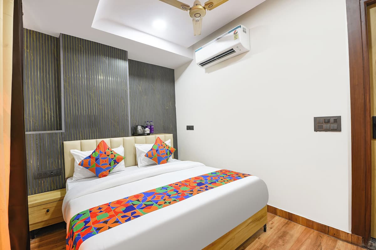 A bedroom with a bed, a ceiling fan, an air conditioning unit, and a wooden floor.