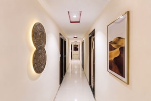 Un pasillo de hotel con diseño moderno, que presenta un largo corredor, iluminación decorativa en la pared y obras de arte enmarcadas.
