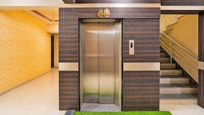 Un ascensor con pantalla digital, una escalera con barandillas metálicas y una pared con diseño a la izquierda.