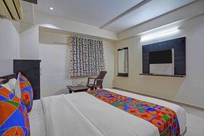 Una habitación de hotel con cama, escritorio, silla, ventana con cortinas y espejo en la pared.