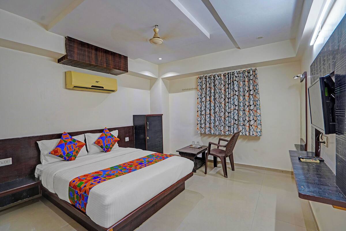 Habitación de hotel con cama, escritorio, silla, televisor y ventana con cortinas estampadas.